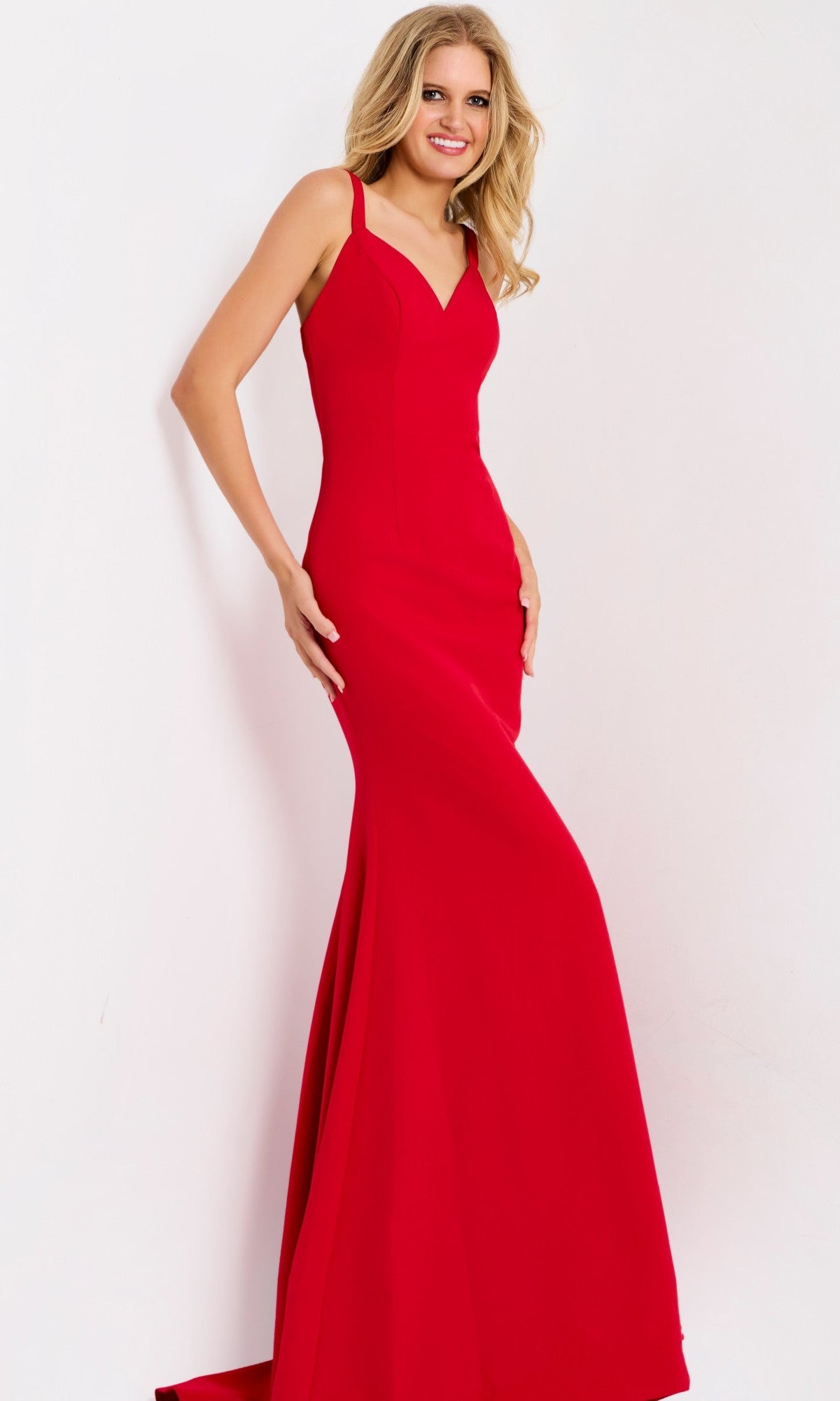A woman wearing the Jovani 49861 long prom dress in red, featuring a sleeveless sheath silhouette and strappy open back, stands smiling against a plain white background.